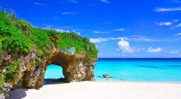 Traumhafter Strand mit Felsentor auf der Okinawa Insel. Türkises Meer und weißer Sand unter blauem Himmel.