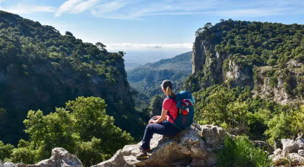 Wanderer mit Rucksack auf Felsen sitzend, genießt die Aussicht auf ein tiefes Tal auf dem Mallorca Fernwanderweg.