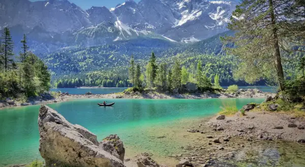 Türkisblaue Bergseen mit einem Kajakfahrer, umgeben von grünen Wäldern und schneebedeckten Gipfeln. Perfekte ausflugsziele bayern für Naturliebhaber.