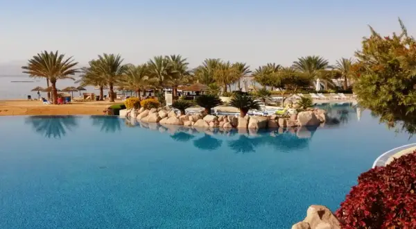 Ein Infinity-Pool mit Blick auf das jordanische Meer, Palmen und einen Sandstrand.
