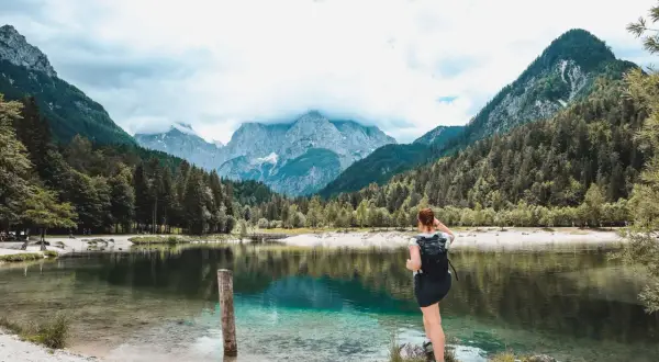 Frau mit Rucksack genießt den Ausblick auf den Jasna See und die Berge. Perfekt für Kranjska Gora Wandern.