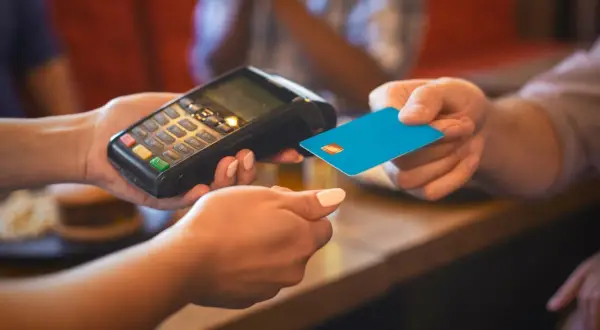 Eine Person bezahlt mit einer blauen Karte an einem Terminal. Das ist eine typische Transaktion, wenn man in Frankreich Geld ausgibt.