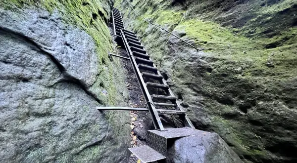 Steile Metalltreppe führt durch eine enge Felsspalte, Moos bedeckt die Wände. Eine leichte Schrammsteine Wanderung mit Ausblick.