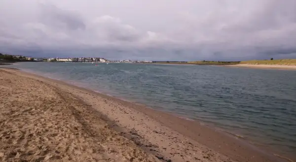 Sandiger Strand mit Blick auf eine Stadt und einen Yachthafen. Der Himmel ist bewölkt, aber das Wasser am Emden Strand ist ruhig.