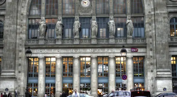 Prachtvolle Fassade des **Paris Nord Bahnhof** mit Statuen und einer Uhr. Autos und Menschen beleben den Vorplatz.