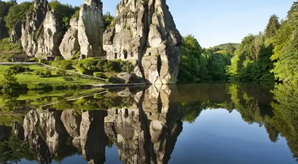 Felsformationen mit kleinen Höhlen spiegeln sich in einem ruhigen See. Ein idyllischer Ort für eine Wanderung im Teutoburger Wald.