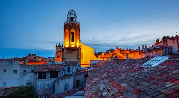 Aix-en-Provence Geheimtipps: Ein beleuchteter Kirchturm ragt über die Dächer der Altstadt im Abendlicht.