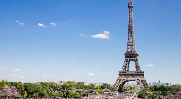 Eiffelturm, ein Paris must see, ragt in den blauen Himmel. Menschen genießen den sonnigen Tag im Park.