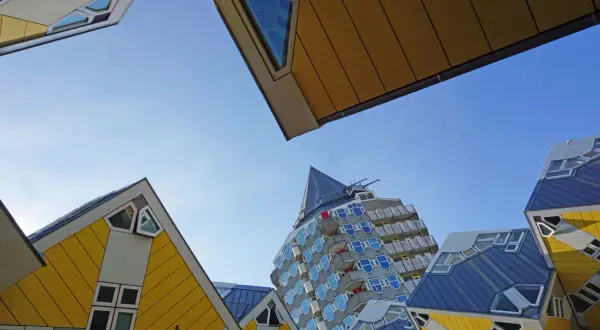 Rotterdam Geheimtipps: Schräge Würfelhäuser und ein futuristisches Hochhaus unter blauem Himmel.
