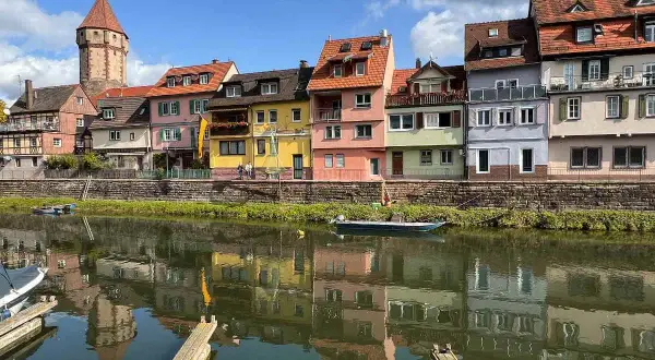 Bunte Häuserfront am Flussufer, ein Turm ragt empor. Hier könnte das Taubertal sein, mit Spiegelungen im Wasser.