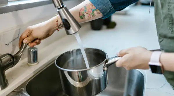 Eine Hand dreht den Wasserhahn auf, um einen Topf mit Leitungswasser aus Budapest zu füllen.