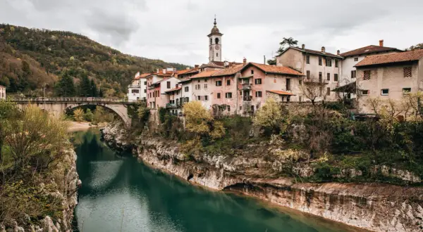 Idyllisches Dorf am Fluss Soča in Slowenien, mit einer Brücke und traditionellen Häusern, die sich an den Hang schmiegen.