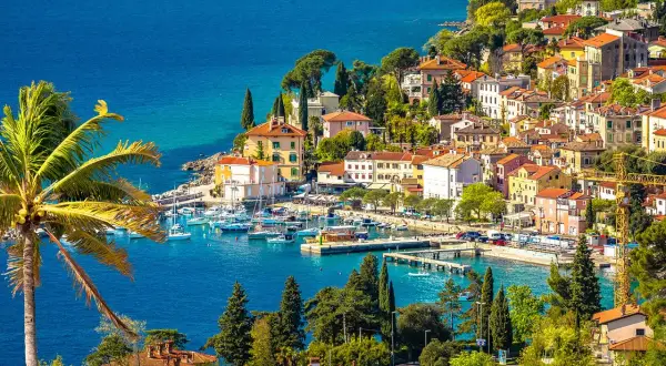 Bunte Häuser am Meer, Boote im Hafen und eine Palme – ein malerischer Blick auf Opatija, der Lust auf Entdeckungen macht. Hier gibt es viele Opatija Geheimtipps zu entdecken.
