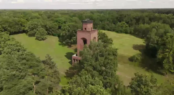 Ein roter Backsteinturm ragt aus einer grünen Wiese im Spreewald, umgeben von üppigen Bäumen.