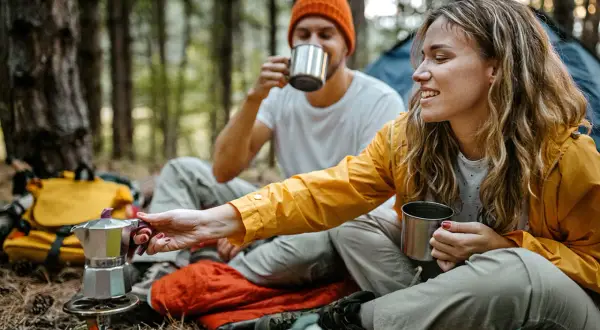 Ein Paar genießt Kaffee aus Metallbechern im Wald. Tolle Mikroabenteuer Ideen für eine Auszeit in der Natur.