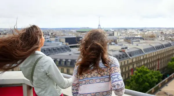 Zwei Teenager genießen den Blick über Paris. Der Wind spielt mit ihren Haaren, während sie die Stadt und den Eiffelturm bestaunen.