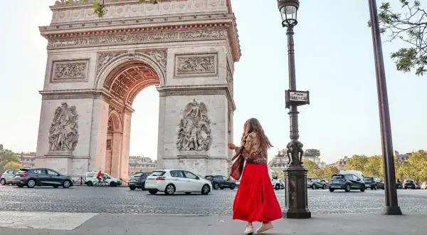 Frau in rotem Kleid tanzt vor dem Arc de Triomphe in Paris.