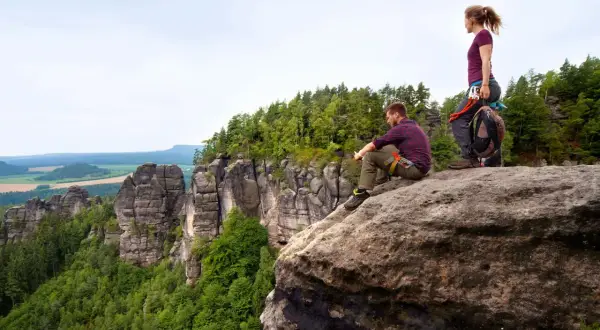 Zwei Kletterer auf den Affensteinen genießen die Aussicht. Ein Mann sitzt, eine Frau steht. Kein Hund zu sehen.
