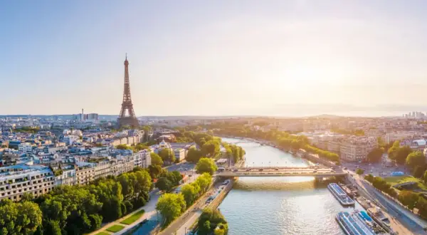 Paris im Sommer: Eiffelturm ragt über die Stadt, die Seine fließt friedlich, Boote liegen am Ufer. Ein malerischer Ausblick.