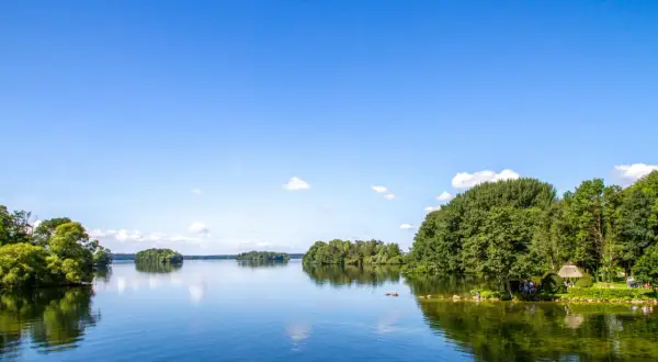 Idyllische Seenlandschaft in Norddeutschland mit grünen Ufern, Inseln und einem klaren blauen Himmel.
