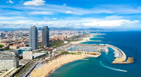 Blick auf den belebten barcelona strand mit Yachten im Hafen und der Skyline der Stadt im Hintergrund.