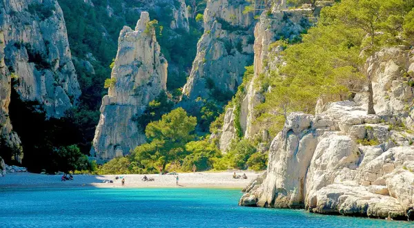 Sonnige Bucht mit türkisfarbenem Wasser und Felsen, ideal zum Calanques Baden. Menschen entspannen am Strand.