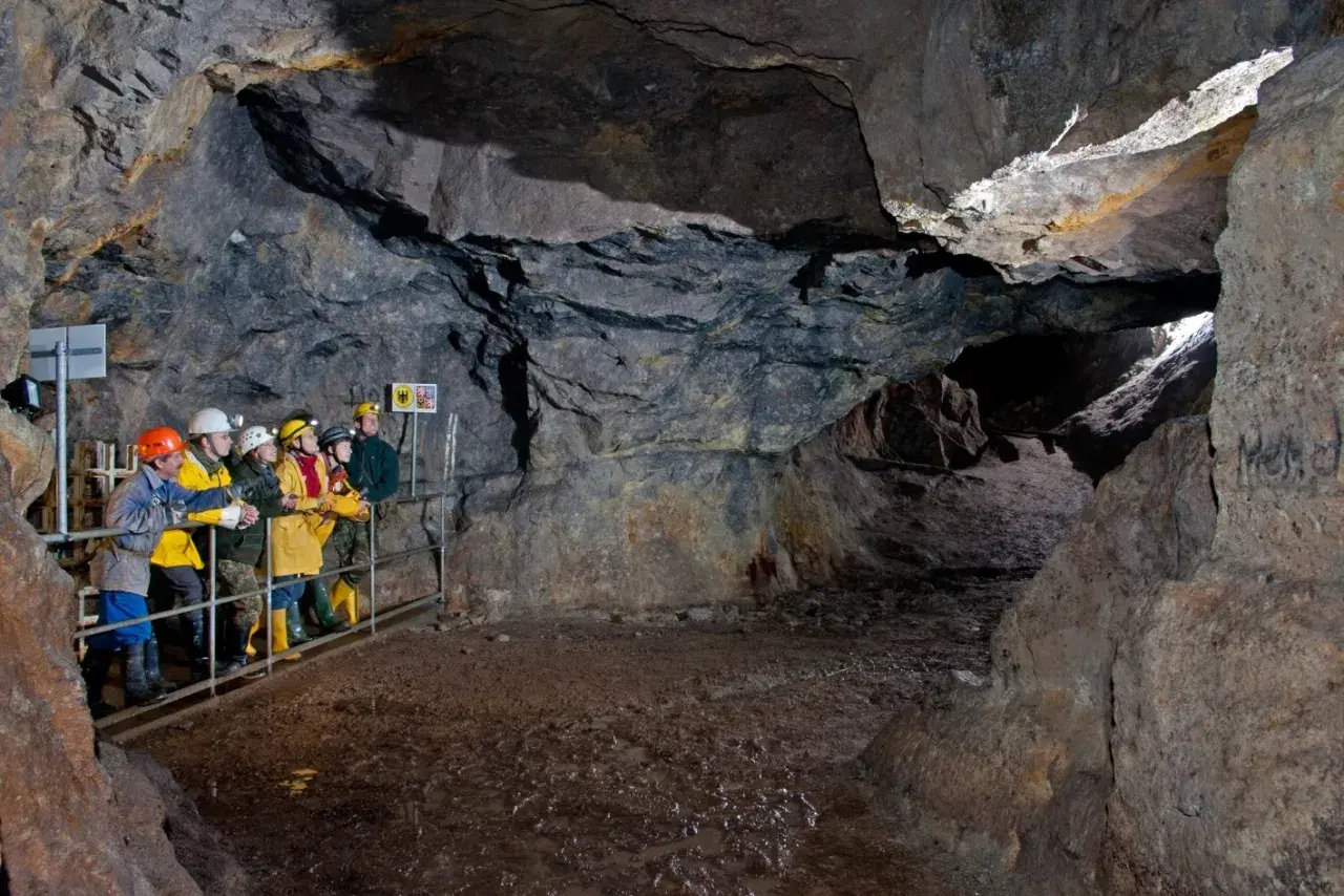 Besucher erkunden eine Höhle im Erzgebirge. Sie tragen Schutzhelme und blicken in die Tiefe des Bergwerks.