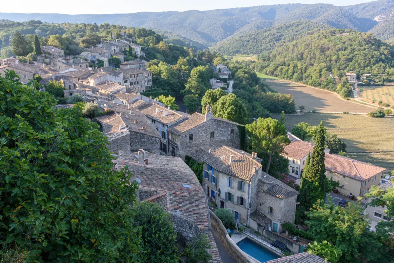 Dächer und Steinhäuser eines Dorfes im Luberon, Provence, eingebettet in grüne Hügel und Felder.