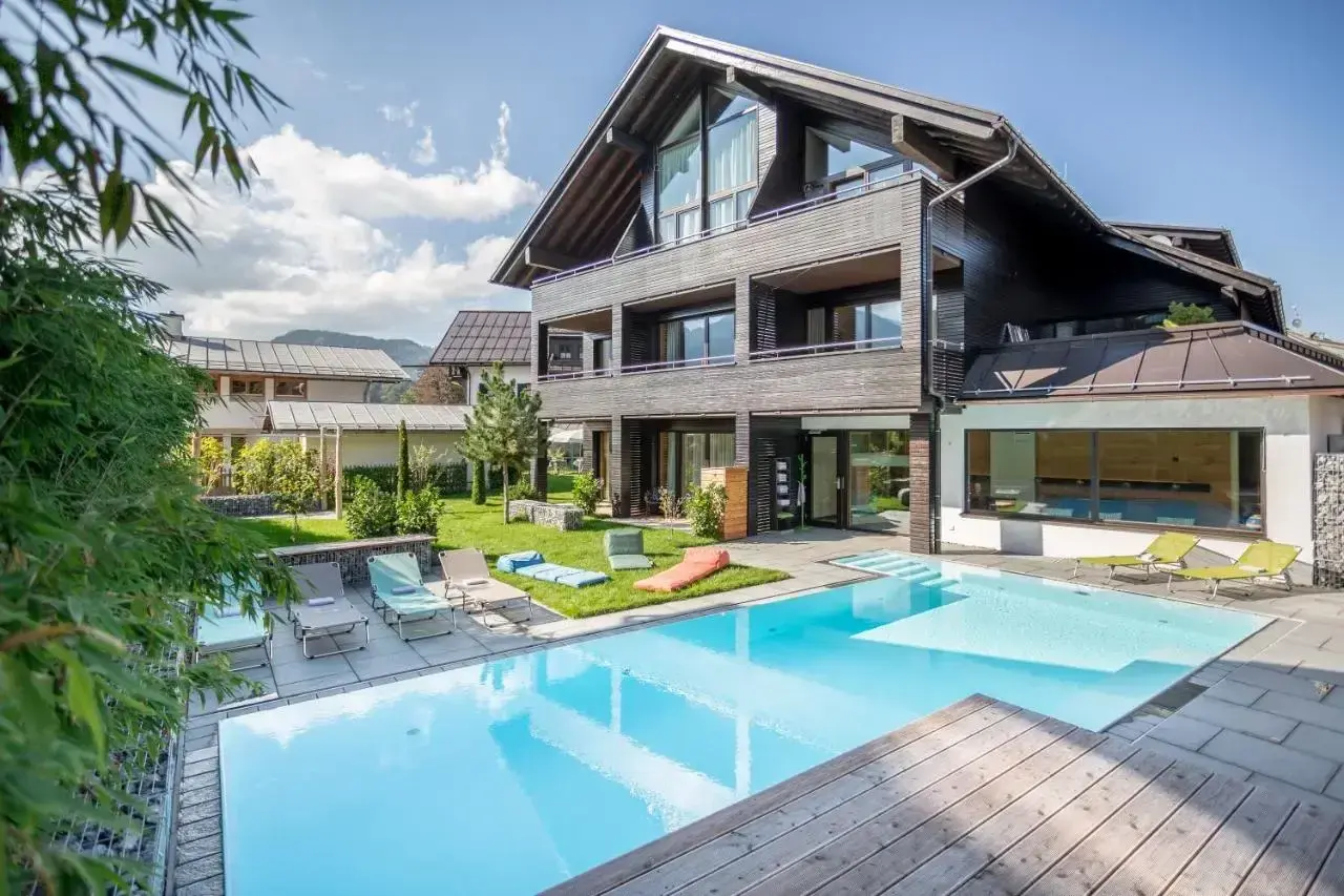 Moderner Poolbereich mit Liegestühlen und Blick auf ein stilvolles Holzhaus. Hier finden Sie die besten Oberstdorf Geheimtipps für Ihren Urlaub.