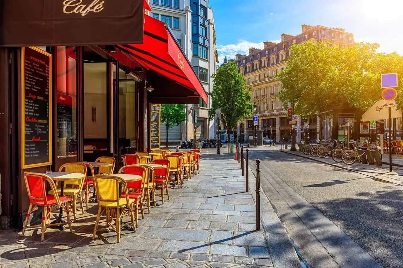Ein sonniger Tag in Oberkampf, Paris. Rote und gelbe Stühle laden vor einem Café zum Verweilen ein.