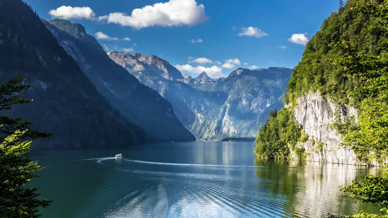 Ein Boot fährt auf einem ruhigen See, umgeben von steilen, bewaldeten Bergen. Ein idyllisches Bild von Badeseen Deutschland.