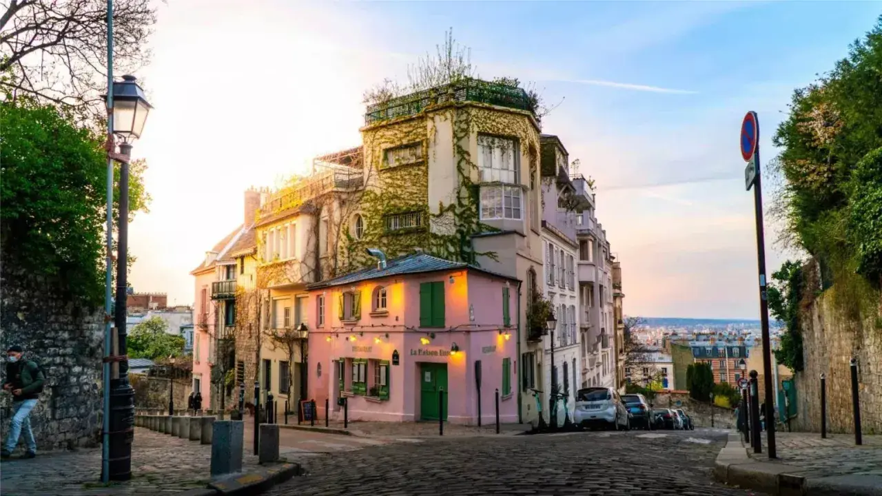 Malerische Gasse in Paris, perfekt für Sightseeing. Ein rosa Restaurant mit grünen Fensterläden und ein Mann mit Maske auf dem Kopfsteinpflaster.