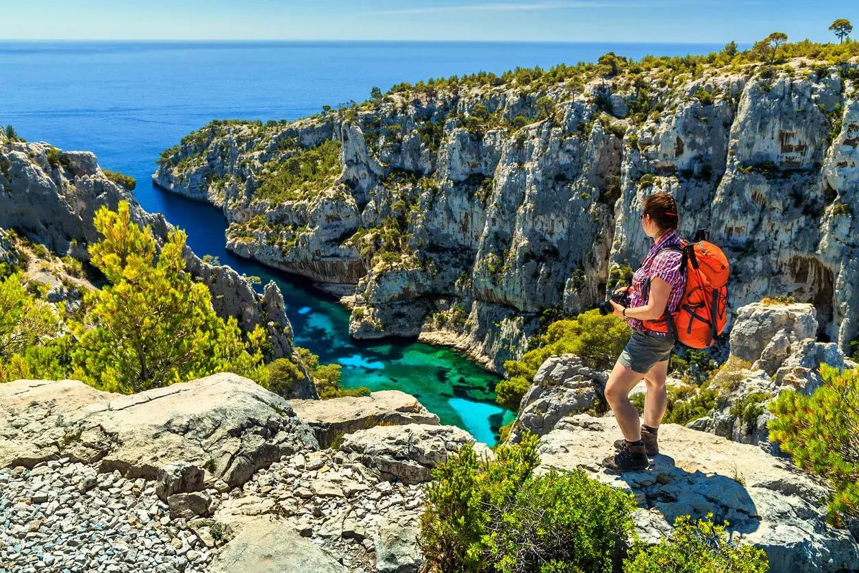 Frau mit Rucksack genießt den Ausblick beim Marseille Wandern. Türkisblaues Wasser in einer Felsbucht.