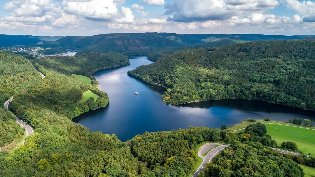 Idyllische Seenlandschaft in der Eifel mit kurviger Straße und einem Schiff. Entdecken Sie diese Eifel Geheimtipps!