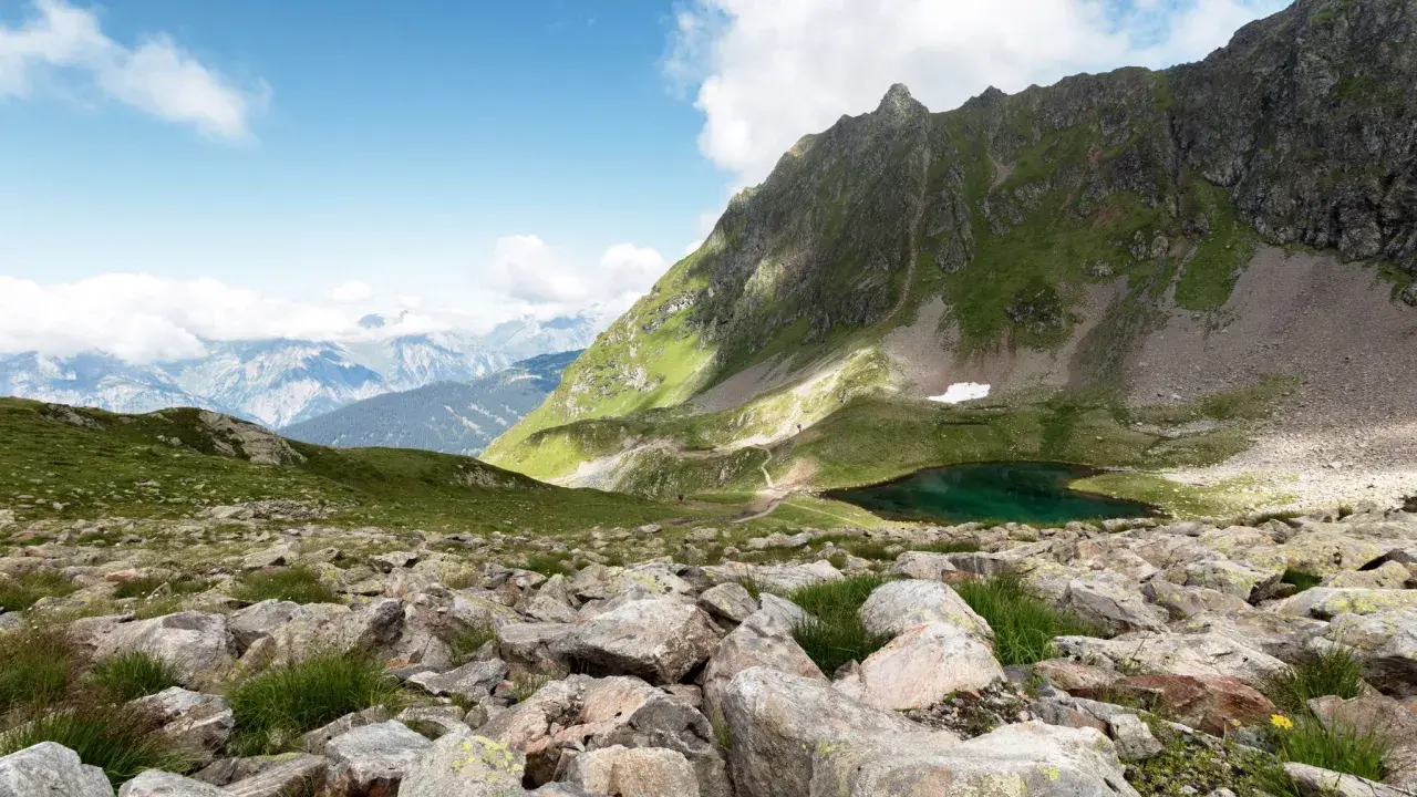 Bergsee bei Schruns, ideal zum Wandern. Grüne Hänge, Felsen und ein tiefblauer Bergsee unter blauem Himmel.