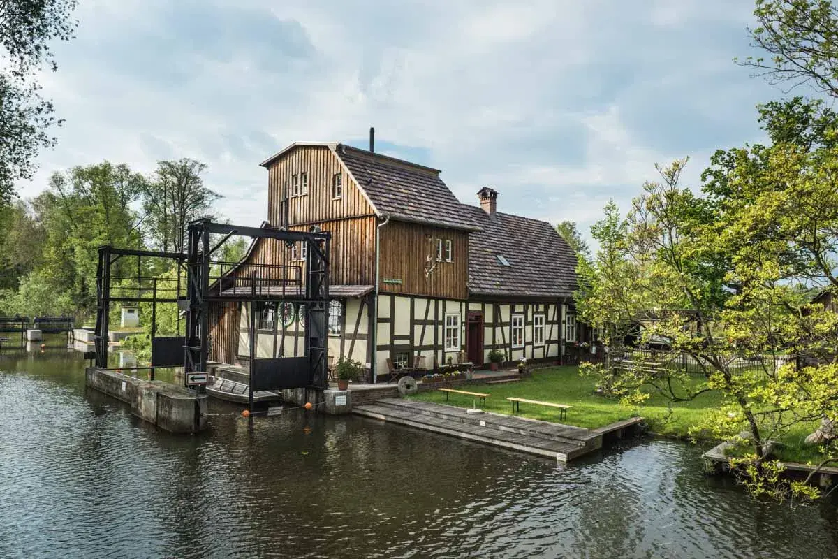 Historische Wassermühle am Wasser, perfekt für einen Spreewald Tagesausflug. Ein idyllischer Ort mit viel Grün und Wasser.