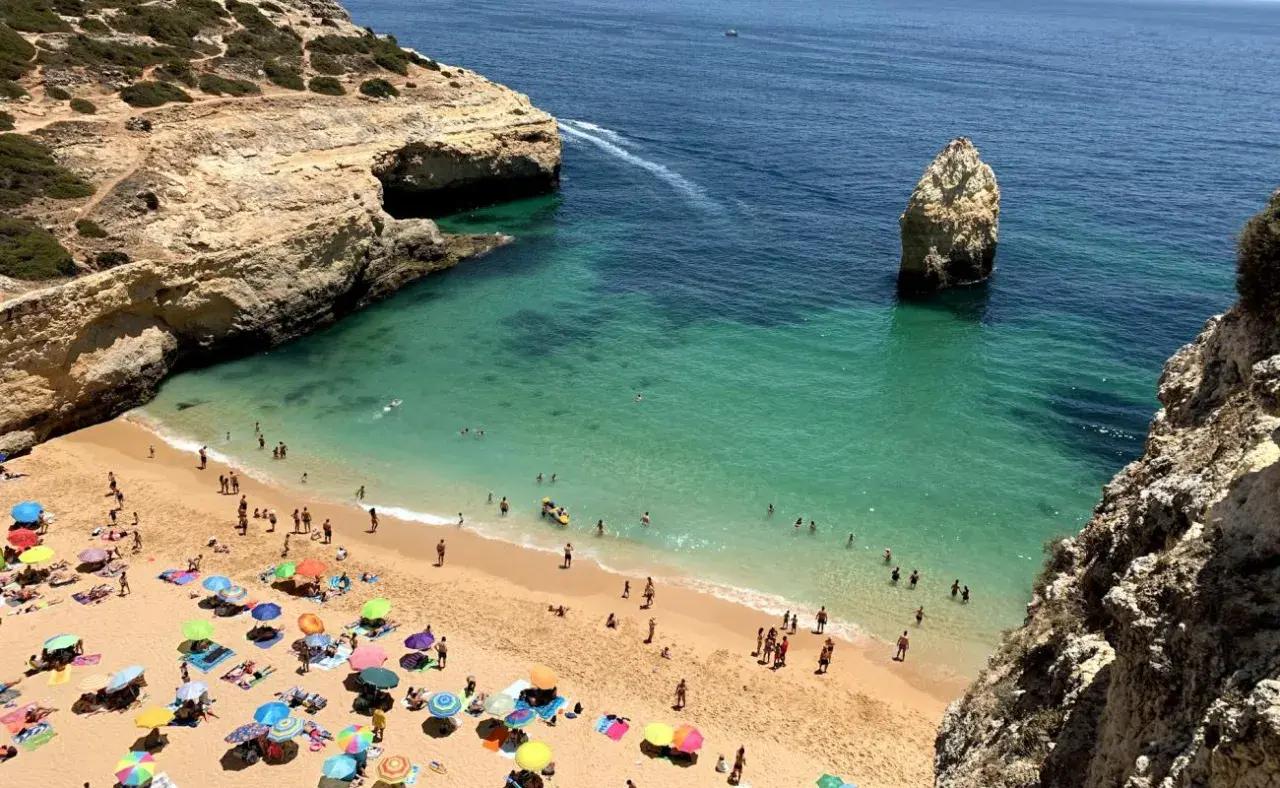 Sonniger Strand an der Algarve, ein echter Geheimtipp mit türkisfarbenem Wasser, Felsen und vielen bunten Sonnenschirmen.
