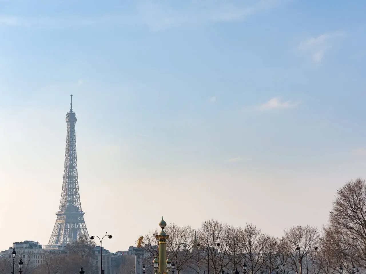 Eiffelturm ragt im winterlichen Paris in den blauen Himmel. Kahle Bäume säumen die Stadt.