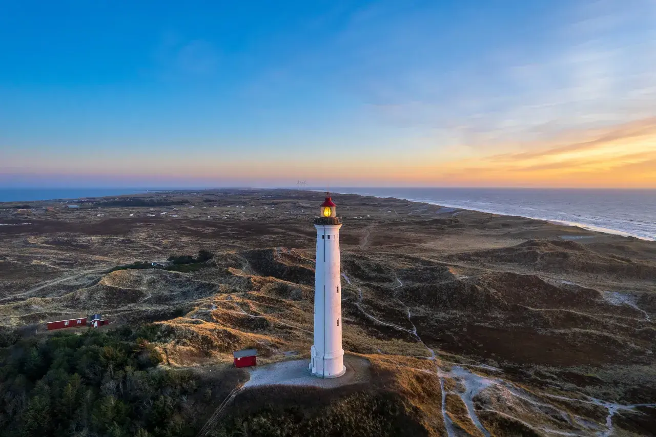 Leuchtturm bei Sonnenuntergang an der Küste, umgeben von Dünen. Ein versteckter Ort, der an Hvide Sande Geheimtipps erinnert.
