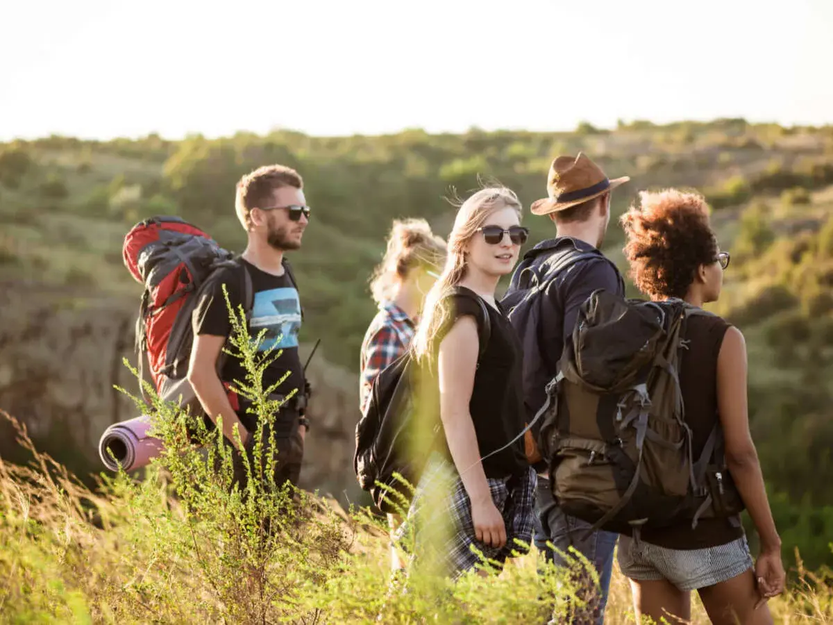 Eine Gruppe junger Leute lernt wandern. Sie tragen Rucksäcke und genießen die Natur bei Sonnenschein.
