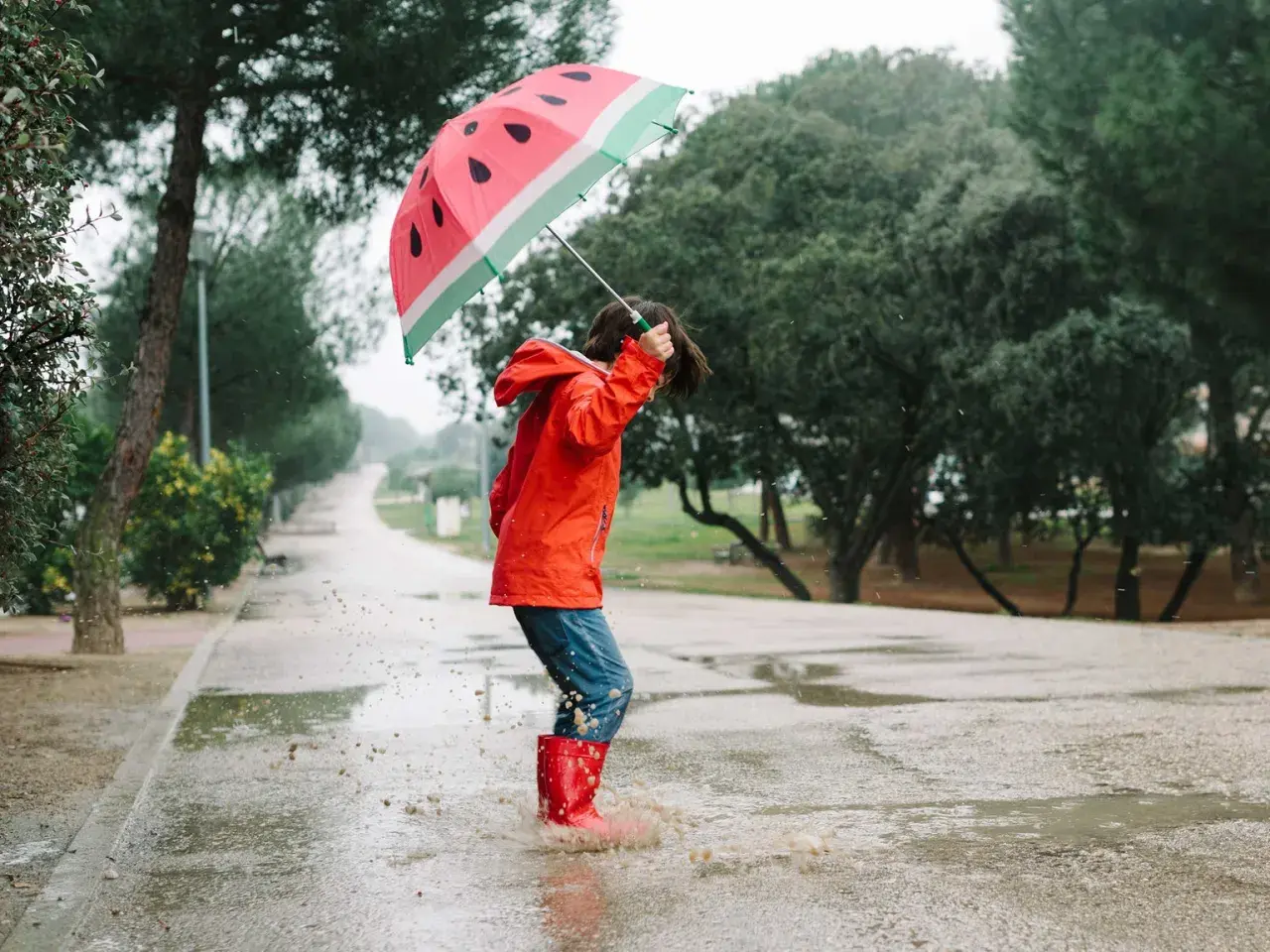 Kind mit Regenschirm und Gummistiefeln springt in Pfütze. Perfekte Freizeit NRW für Regentage.