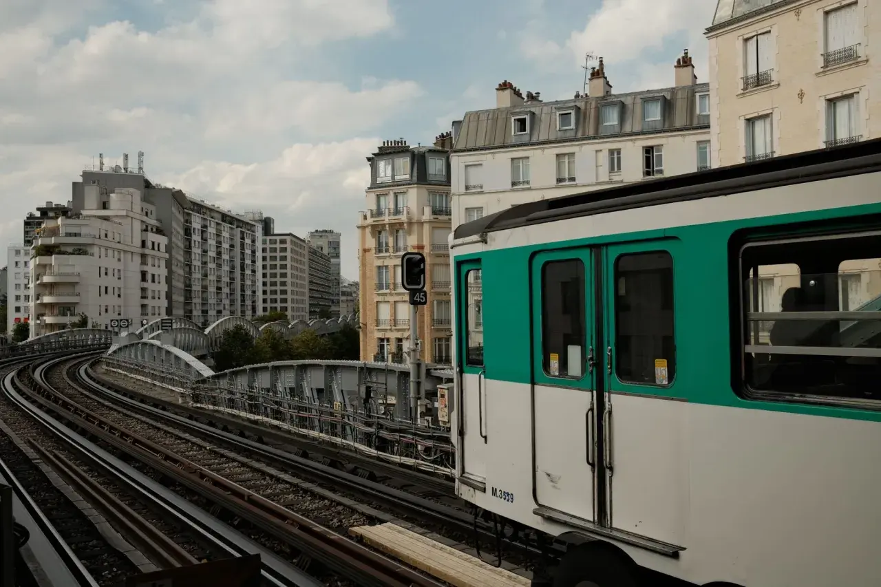 Ein Pariser Métro-Zug fährt auf den Gleisen in Richtung Saint-Lazare. Gebäude und eine Brücke säumen die Strecke.