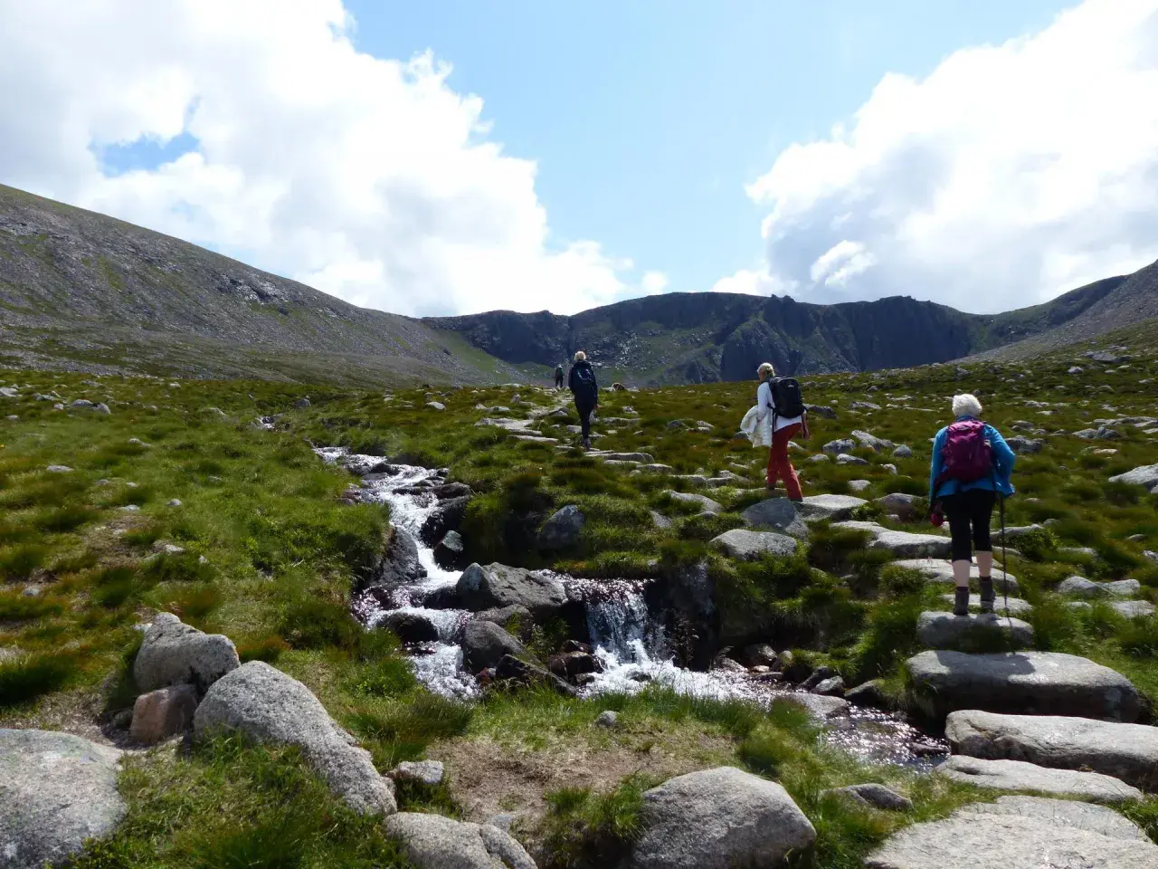Drei Wanderer genießen das Cairngorms National Park Wandern entlang eines steinigen Pfades mit einem plätschernden Bach.