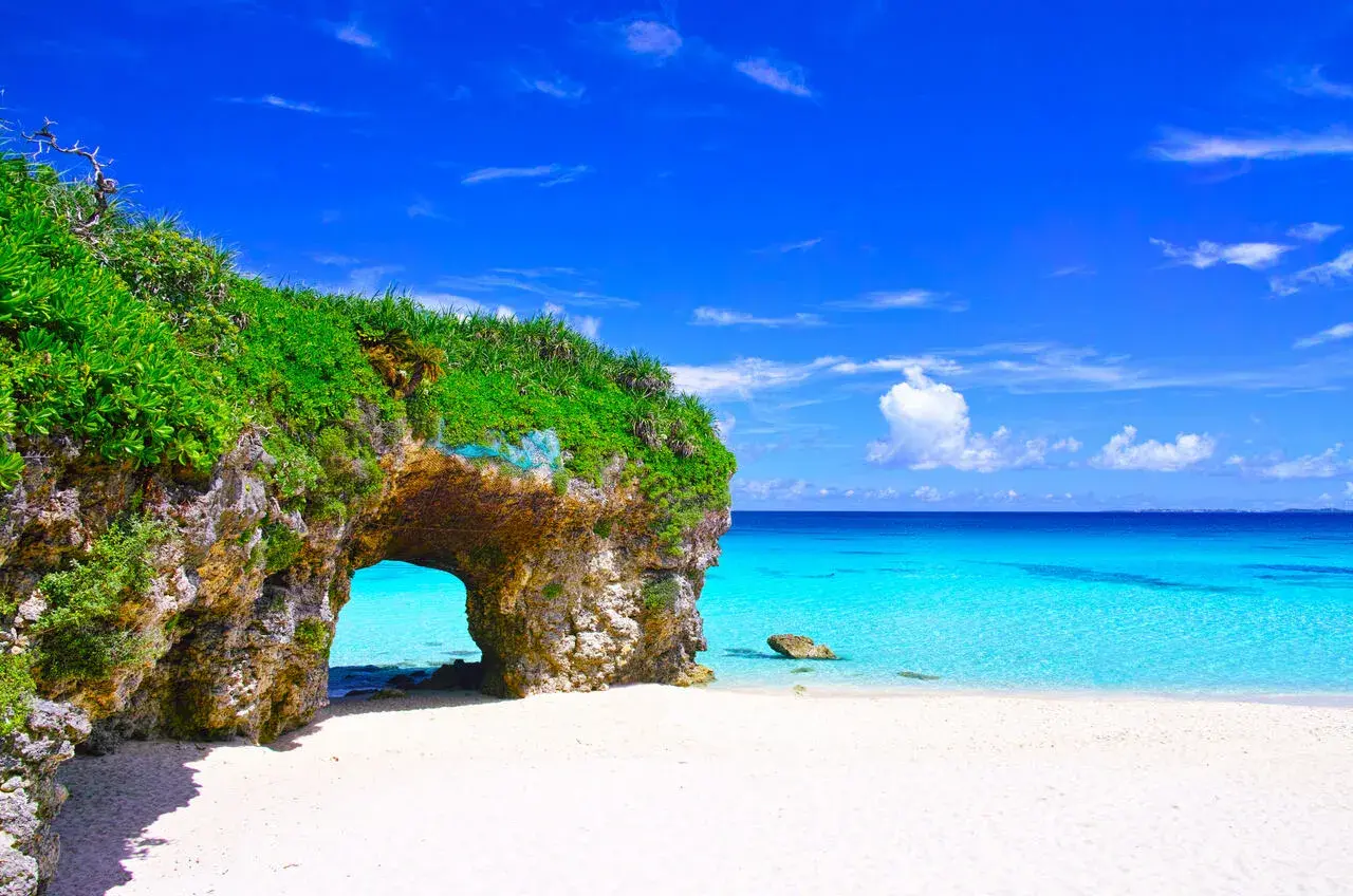 Traumhafter Strand mit Felsentor auf der Okinawa Insel. Türkises Meer und weißer Sand unter blauem Himmel.