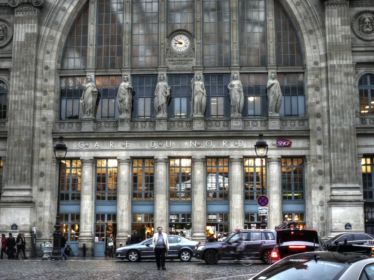 Prachtvolle Fassade des **Paris Nord Bahnhof** mit Statuen und einer Uhr. Autos und Menschen beleben den Vorplatz.