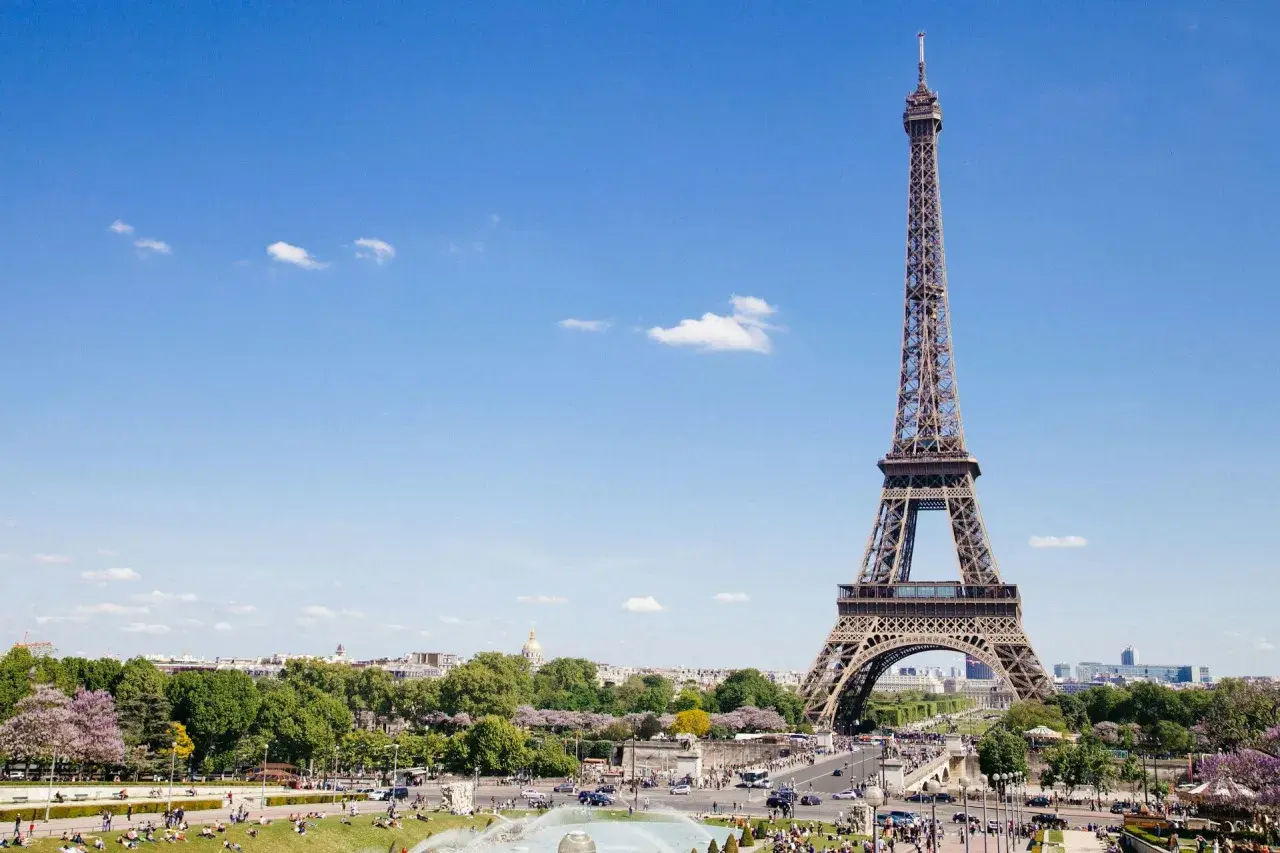 Eiffelturm, ein Paris must see, ragt in den blauen Himmel. Menschen genießen den sonnigen Tag im Park.