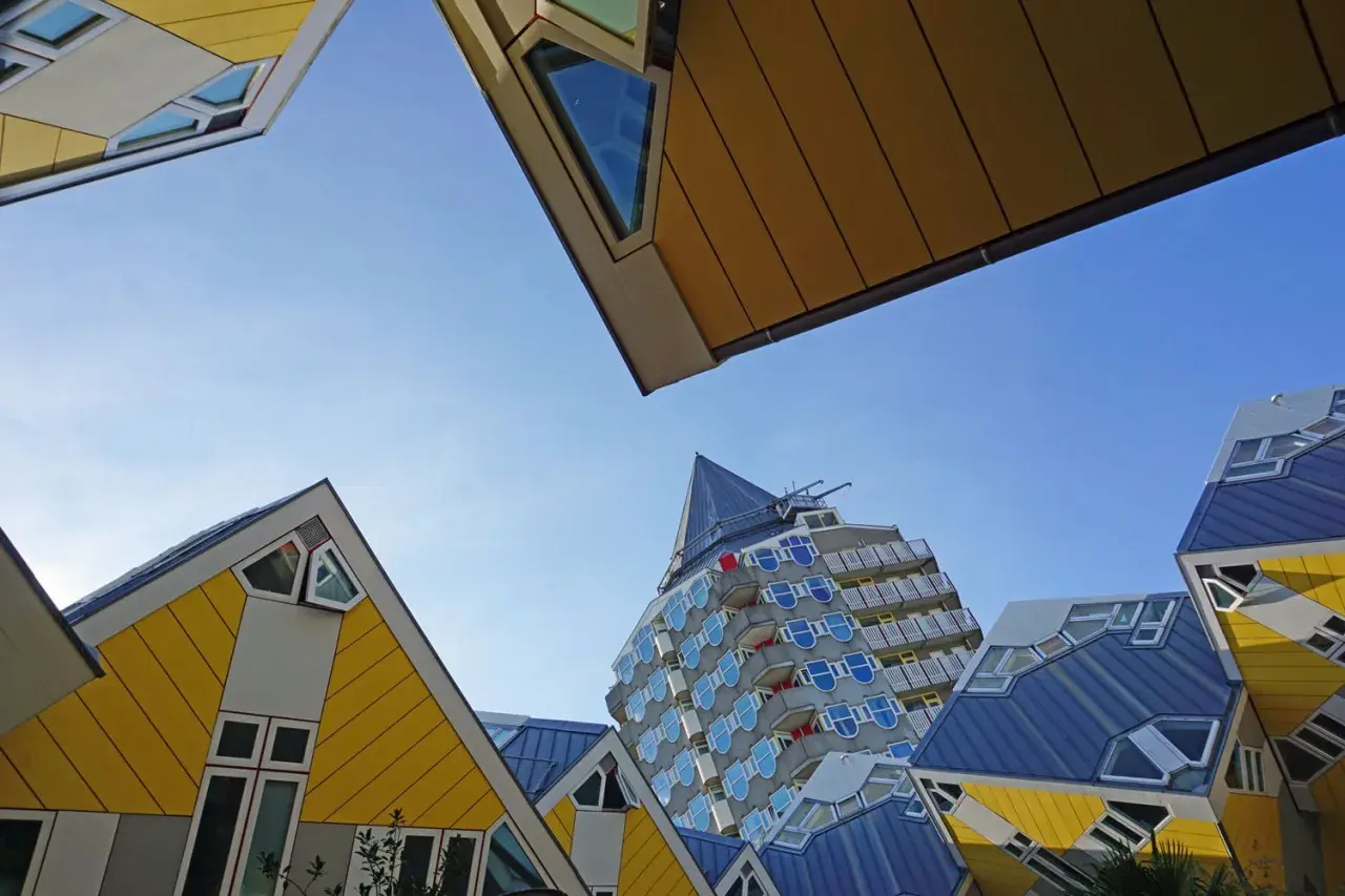 Rotterdam Geheimtipps: Schräge Würfelhäuser und ein futuristisches Hochhaus unter blauem Himmel.