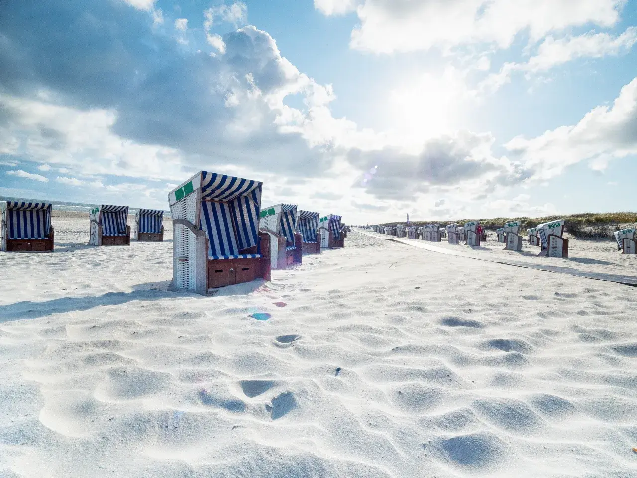 Strandkörbe auf einer autofreien ostfriesischen Insel. Sonnenschein und Wolken über dem weißen Sand.