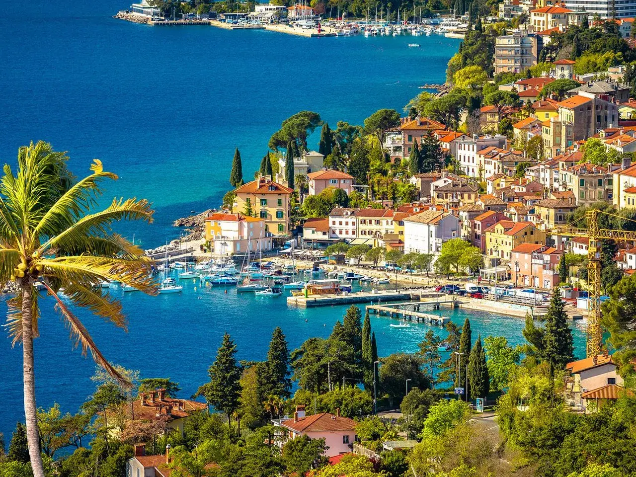 Bunte Häuser am Meer, Boote im Hafen und eine Palme – ein malerischer Blick auf Opatija, der Lust auf Entdeckungen macht. Hier gibt es viele Opatija Geheimtipps zu entdecken.