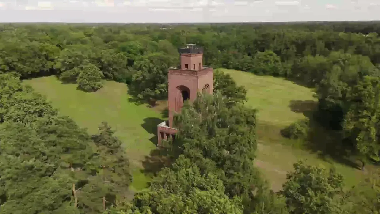 Ein roter Backsteinturm ragt aus einer grünen Wiese im Spreewald, umgeben von üppigen Bäumen.